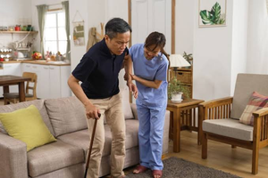 Caregiver helping an elderly man walk with a cane at home